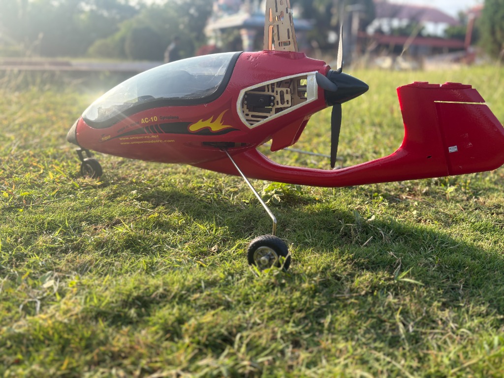 Red custom-built AC-10 Gyroplane model sitting on green grass field